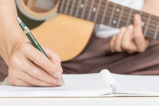 man writing lyrics with an acoustic